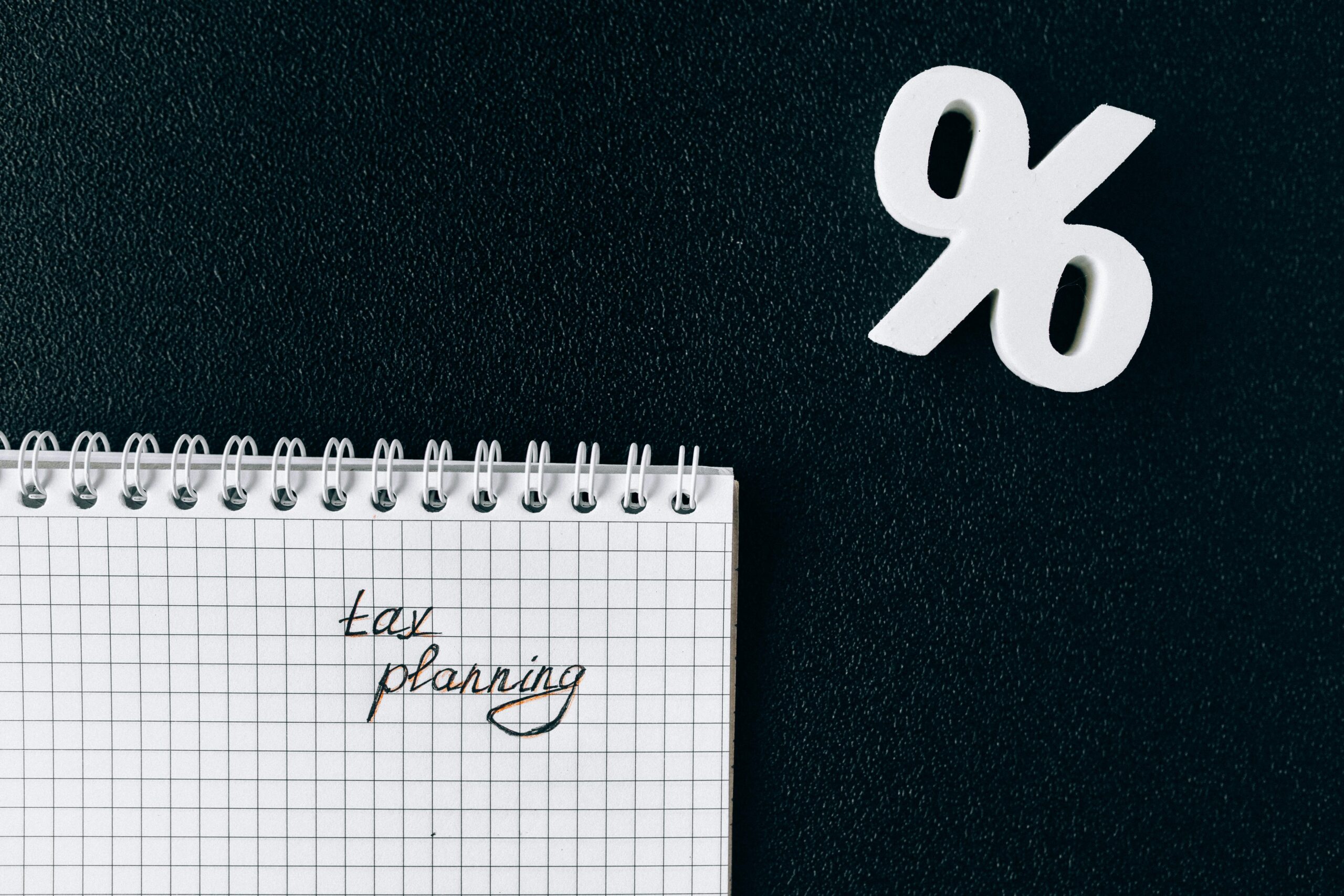 A notebook with 'tax planning' written on a grid paper next to a percent symbol on a black background.